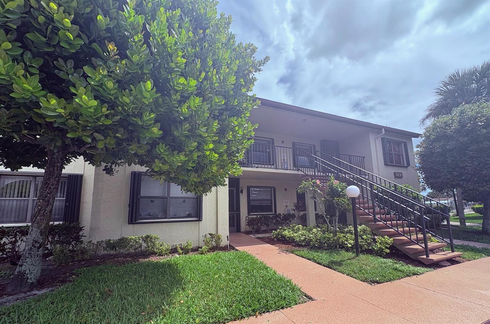 A two-story apartment building features a concrete staircase, a walkway, and mature landscaping — 7831 Willow Spring Drive # 526, Lake Worth FL 33467, LAKE WORTH, FL