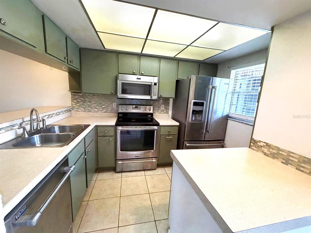 A kitchen features green cabinets, stainless steel appliances, a tiled backsplash, and a drop ceiling — 3128 SIR HAMILTON CIRCLE UNIT 4, TITUSVILLE, FL
