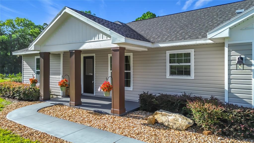 The exterior of a house features a covered porch with brown columns and gray siding — 15204 GANSTER DRIVE, BROOKSVILLE, FL