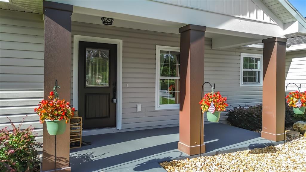 A covered front porch features three brown pillars, light siding, and hanging flower baskets — 15204 GANSTER DRIVE, BROOKSVILLE, FL