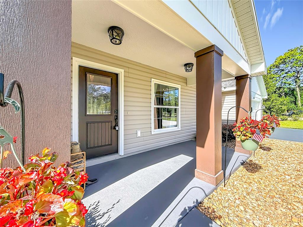 A covered front porch features a dark brown door, light siding, and a square pillar — 15204 GANSTER DRIVE, BROOKSVILLE, FL