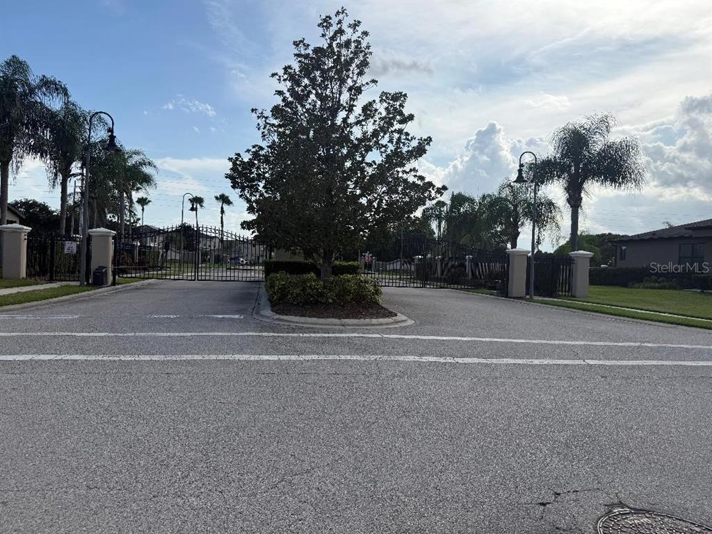 A paved road leads to a gated entrance with a central tree and palm trees — 2432 SEVEN OAKS DRIVE, ST CLOUD, FL