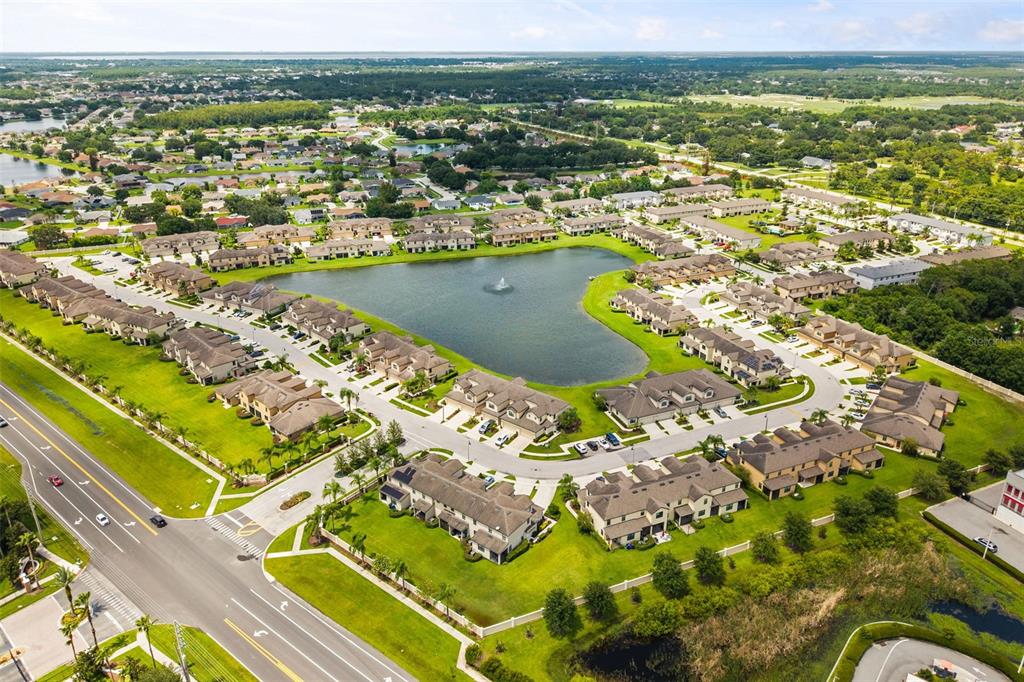 Aerial view of a residential community featuring townhomes surrounding a central lake with a fountain — 2432 SEVEN OAKS DRIVE, ST CLOUD, FL