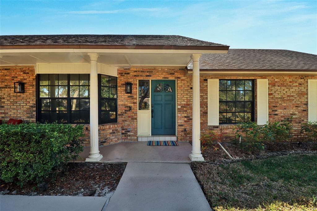 A brick house exterior features a covered porch with white columns and a teal front door — 4318 WOODTREE LANE, ORLANDO, FL