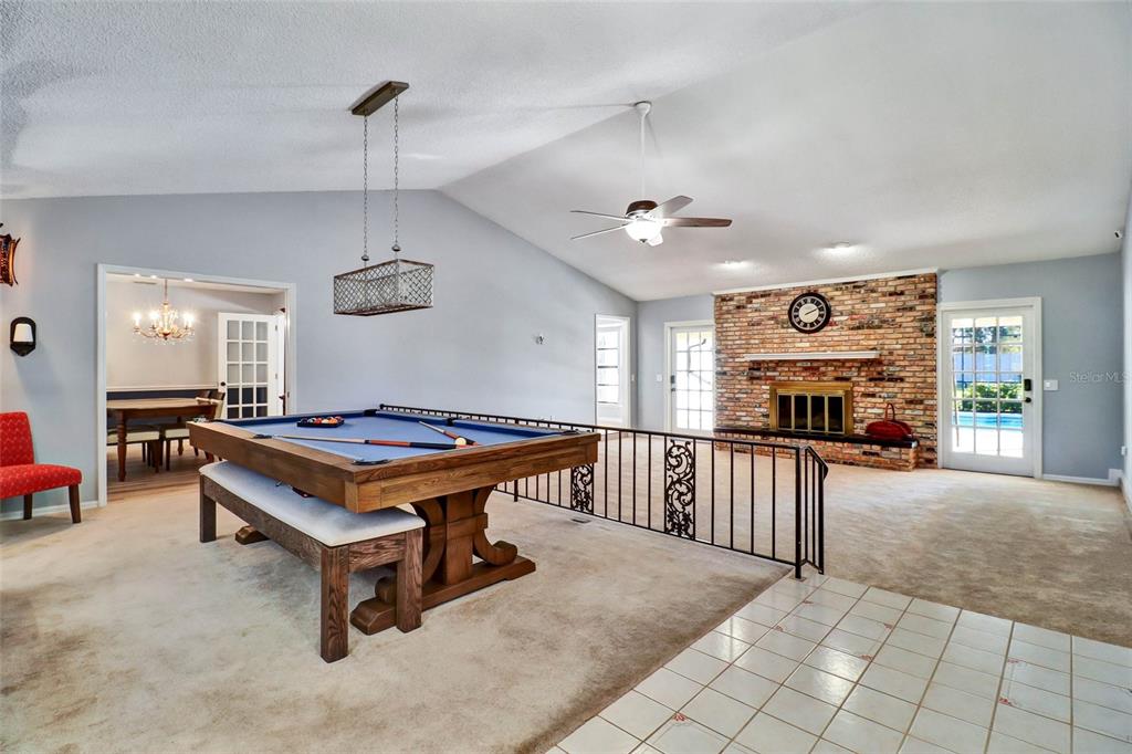 A living room features a pool table, a brick fireplace, and a vaulted ceiling — 4318 WOODTREE LANE, ORLANDO, FL
