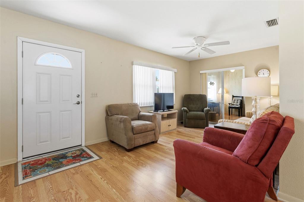 A living room features hardwood floors, a white front door, and several armchairs — 12400 PARK BOULEVARD UNIT 521, SEMINOLE, FL