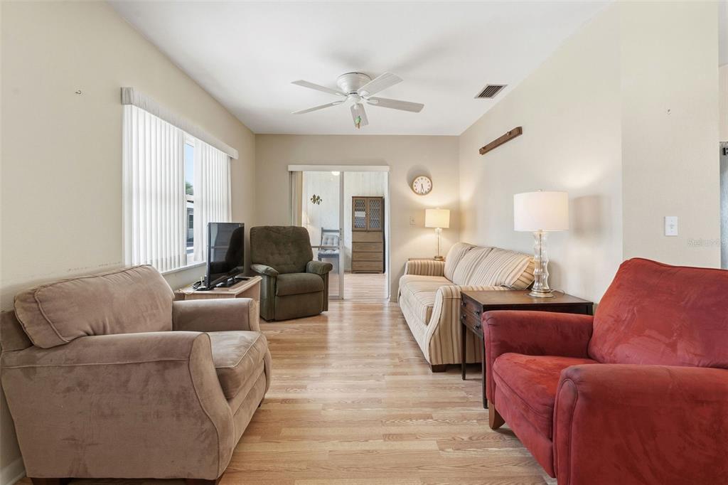 A living room features light wood flooring, a ceiling fan, and multiple pieces of furniture — 12400 PARK BOULEVARD UNIT 521, SEMINOLE, FL