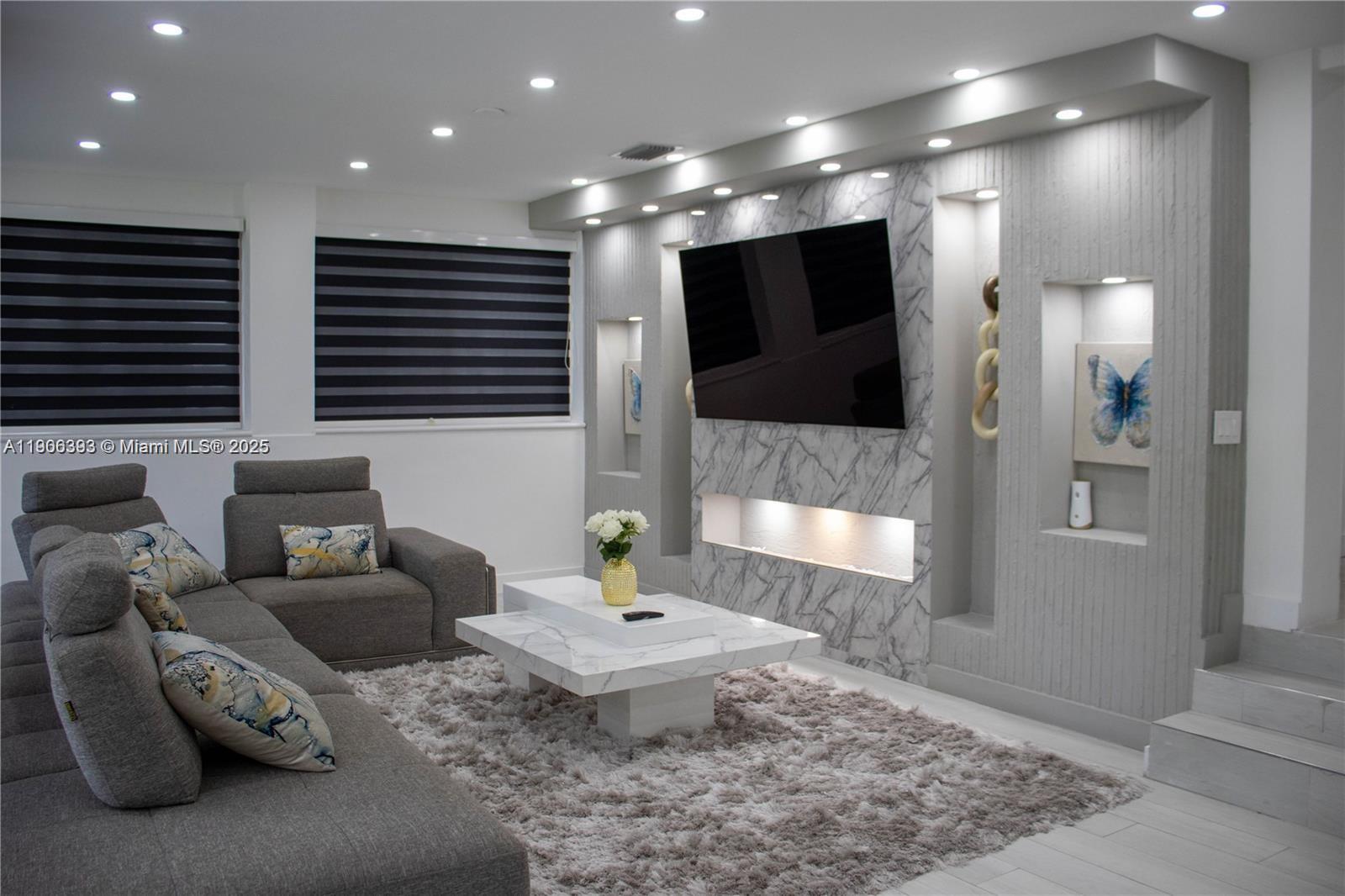 A modern living room features a marble accent wall with a mounted television and fireplace — 295 NE 150th St, Miami FL 33161, MIAMI, FL