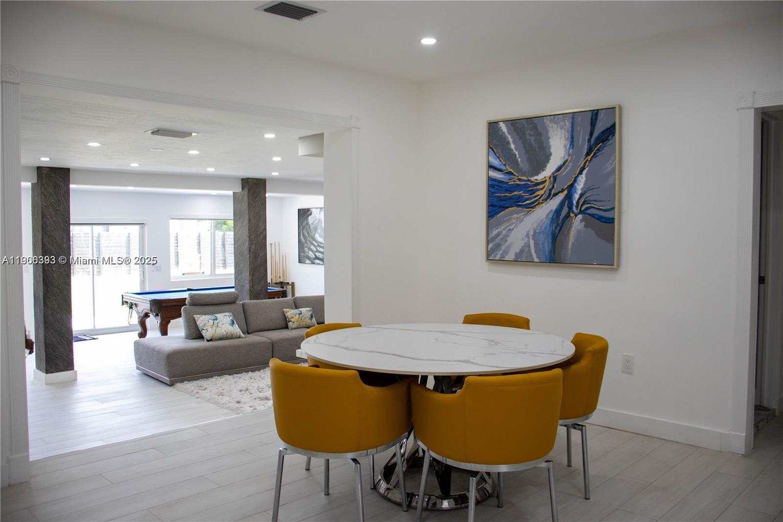 A dining area with a round marble table and yellow chairs overlooks a living room — 295 NE 150th St, Miami FL 33161, MIAMI, FL