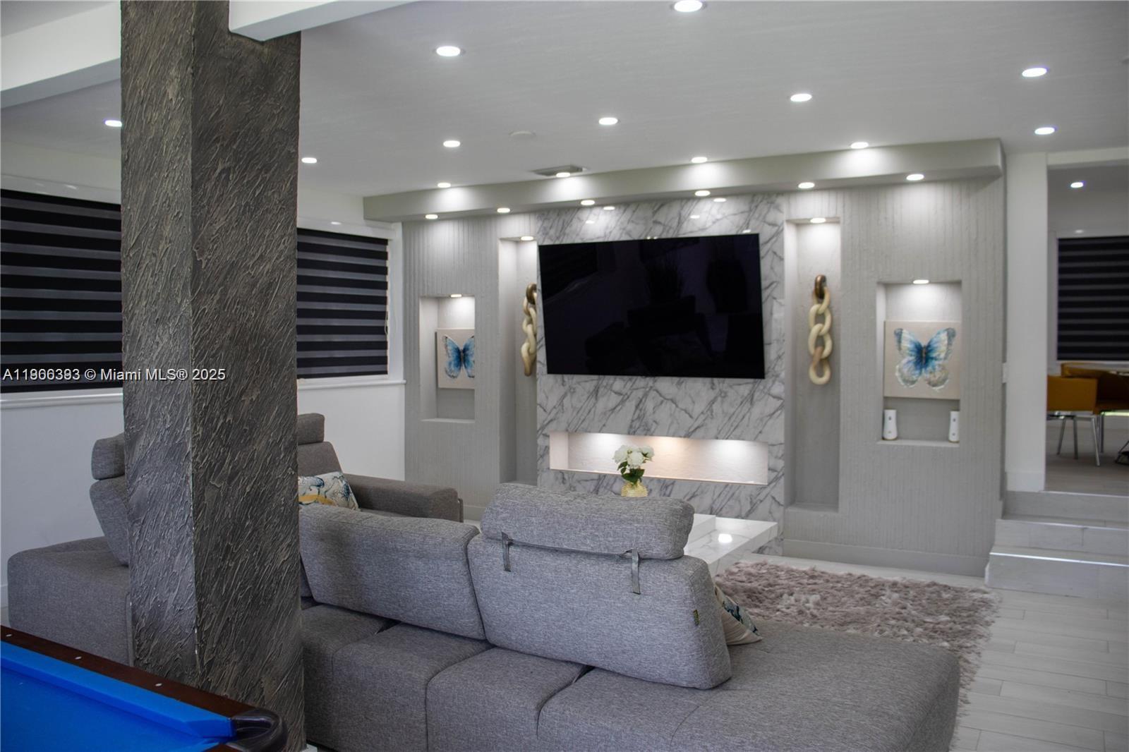 A living room features a marble-accented media wall with recessed shelving and a grey sectional — 295 NE 150th St, Miami FL 33161, MIAMI, FL