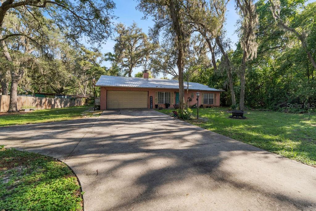 A single-story house with a metal roof and a concrete driveway surrounded by trees — 38213 PALM GROVE DRIVE, ZEPHYRHILLS, FL