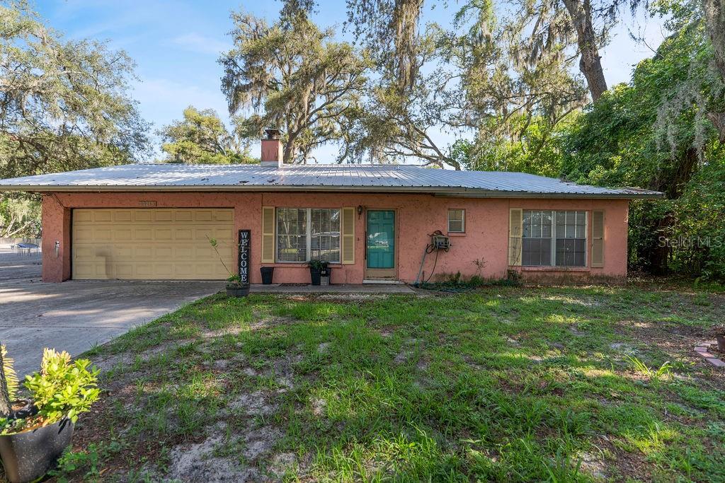 A single-story, pink-stucco house with a metal roof, a two-car garage, and a front yard — 38213 PALM GROVE DRIVE, ZEPHYRHILLS, FL