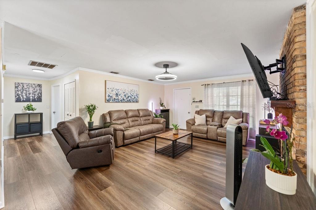 A living room features brown leather furniture, wood-look flooring, and a brick fireplace wall — 38213 PALM GROVE DRIVE, ZEPHYRHILLS, FL