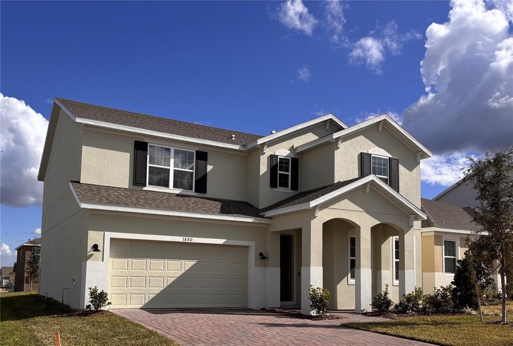 A two-story suburban house features a beige stucco exterior, a two-car garage, and a driveway — 1880 ROSS HAMMOCK AVENUE, GROVELAND, FL