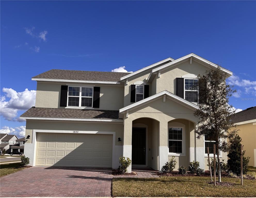 A two-story suburban house features a beige stucco exterior, a two-car garage, and a paved driveway — 1880 ROSS HAMMOCK AVENUE, GROVELAND, FL