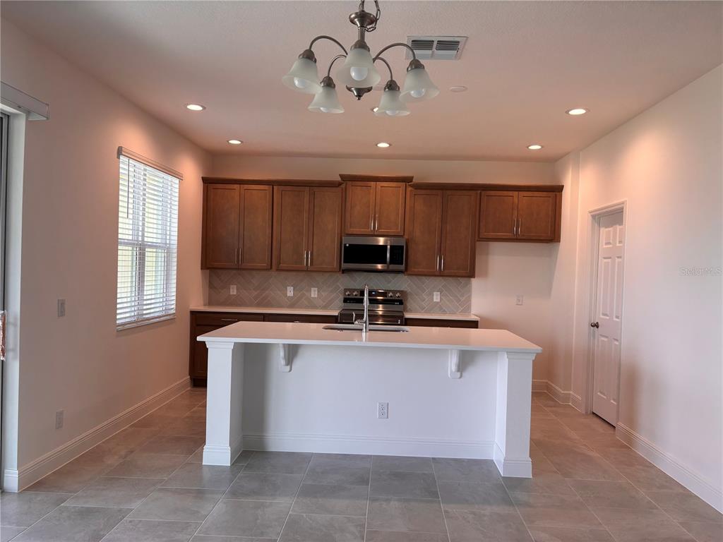 A kitchen features wooden cabinets, a white island, stainless steel appliances, and tile flooring — 1880 ROSS HAMMOCK AVENUE, GROVELAND, FL