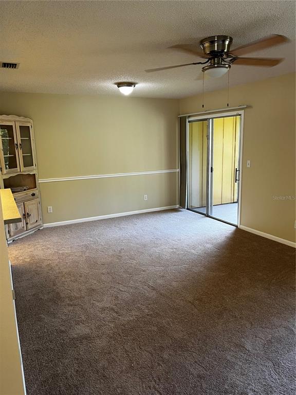 A carpeted living room features a ceiling fan, a corner hutch, and sliding glass doors — 120 HIBISCUS WOODS COURT UNIT 11B, DELTONA, FL