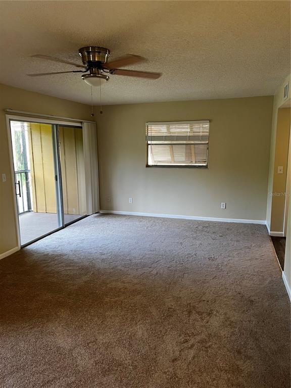 An empty living room features beige carpet, a ceiling fan, and a sliding glass door — 120 HIBISCUS WOODS COURT UNIT 11B, DELTONA, FL