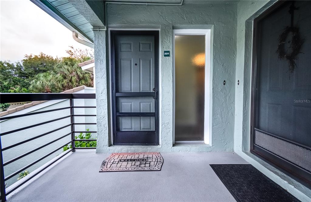 A covered entryway features a gray front door with a screen door and a welcome mat — 600 CARRIAGE HOUSE LANE UNIT 201, NOKOMIS, FL