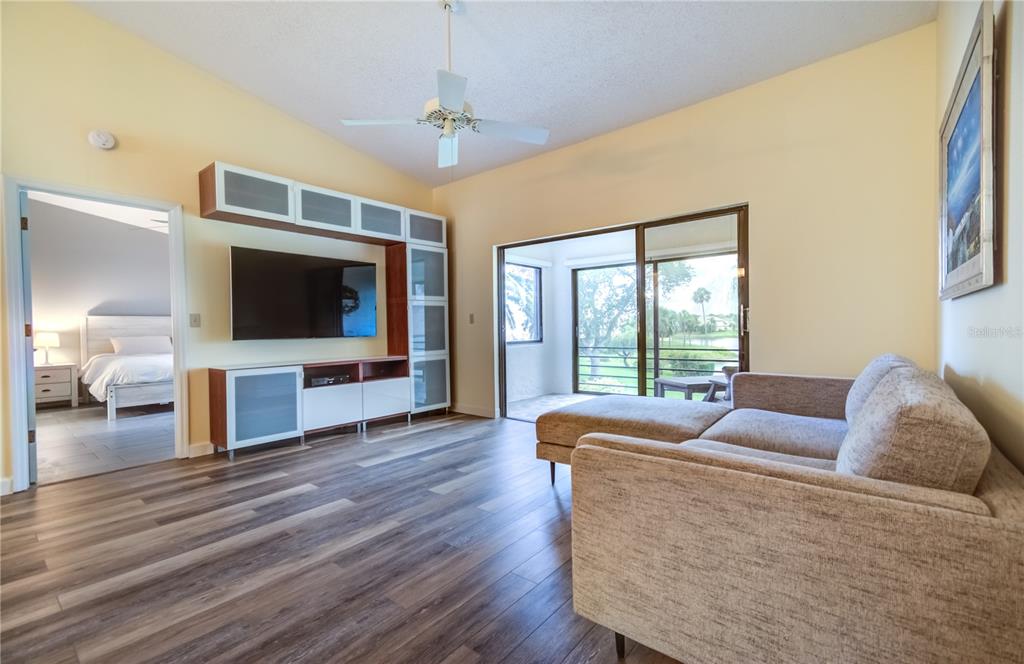 A living room with wood-look flooring, a wall-mounted television, and a sliding door to a balcony — 600 CARRIAGE HOUSE LANE UNIT 201, NOKOMIS, FL