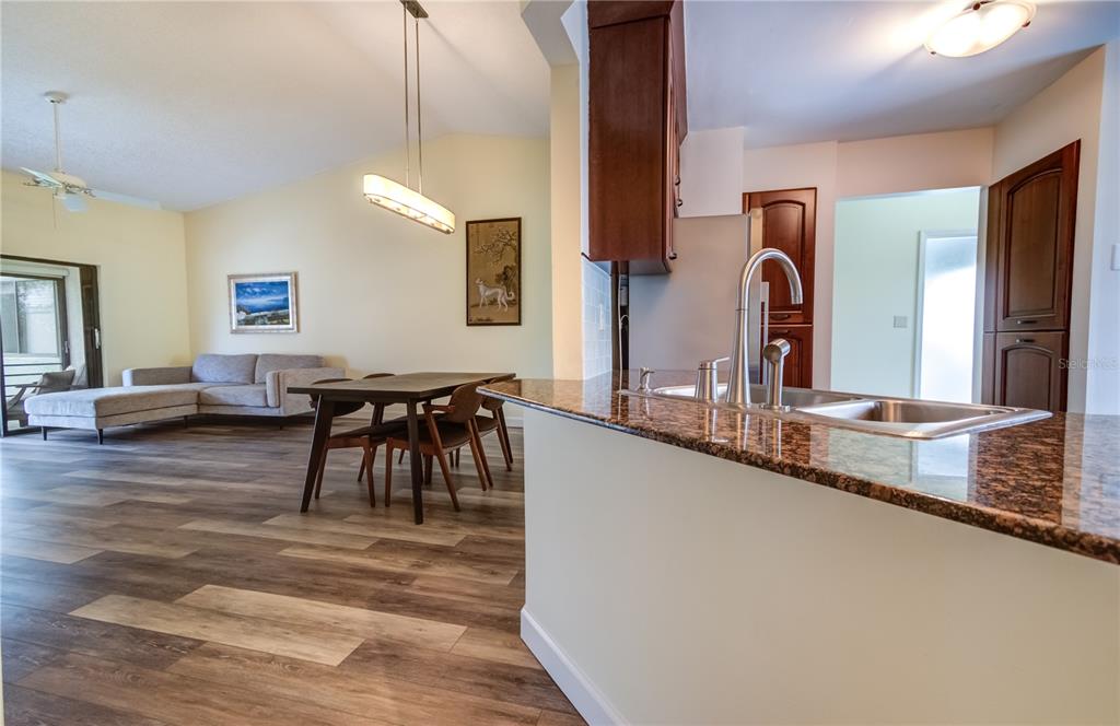 A kitchen with granite countertops overlooks a dining area and living room with wood flooring — 600 CARRIAGE HOUSE LANE UNIT 201, NOKOMIS, FL