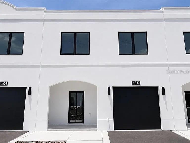 The exterior of a modern white townhouse features black garage doors and matching window frames — 4365 CAMBIO GARDENS COURT, TAMPA, FL