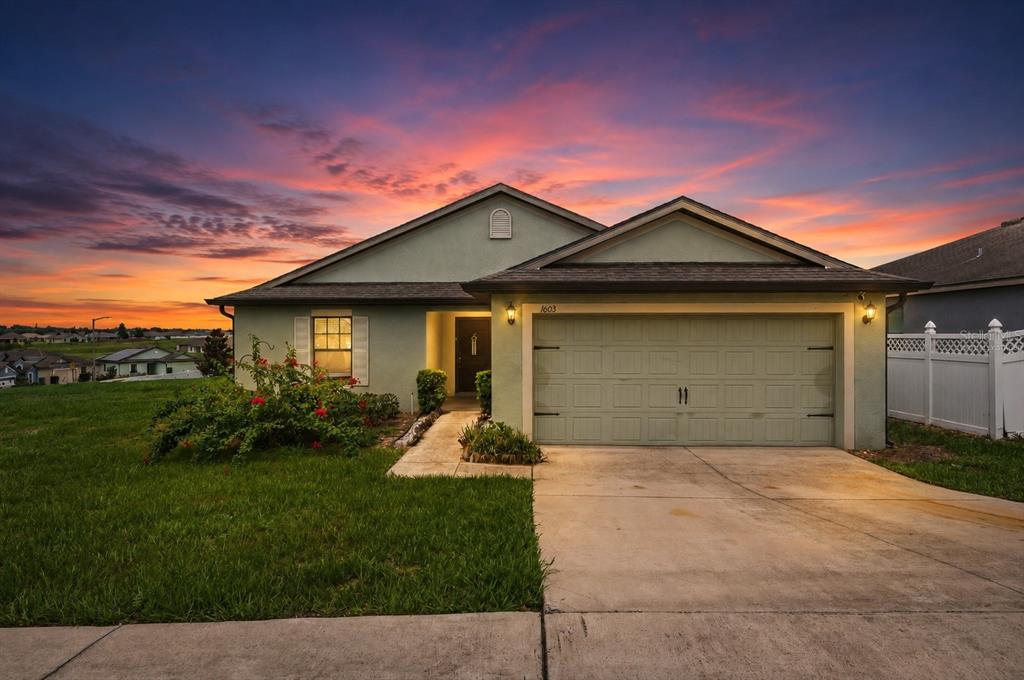 A single-story house with a green stucco exterior, a two-car garage, and a sunset sky — 1603 ELLINGTON DRIVE, DUNDEE, FL