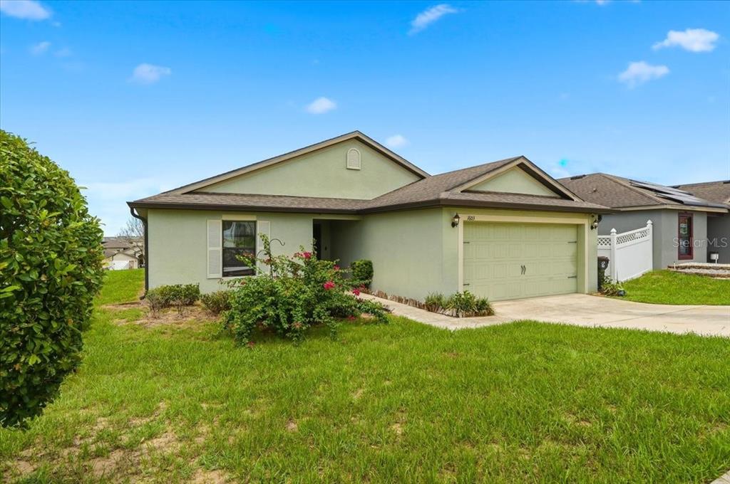 A single-story house with light green stucco siding, a two-car garage, and a front lawn — 1603 ELLINGTON DRIVE, DUNDEE, FL