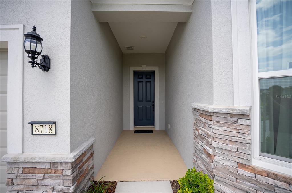A covered entryway features a dark blue front door, stone accents, and a wall-mounted lantern — 8718 SW 59TH LANE ROAD, OCALA, FL