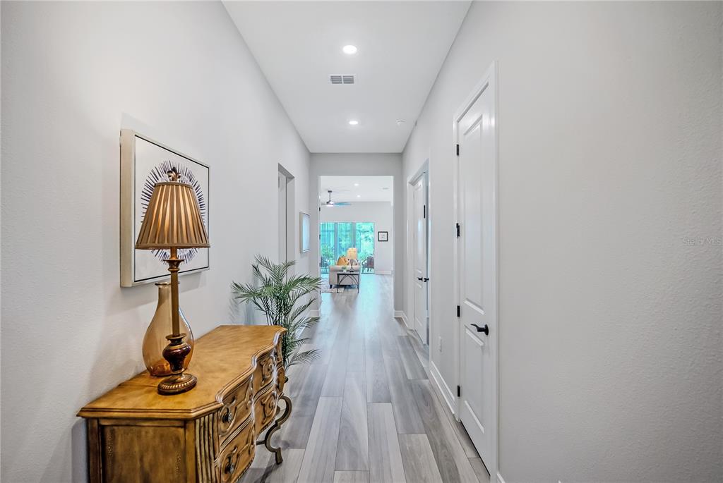 A hallway with wood-look flooring leads from a foyer toward a bright living area — 8718 SW 59TH LANE ROAD, OCALA, FL