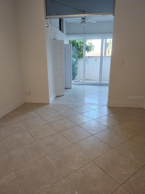 A room with beige tile flooring leads through an open doorway to a sunroom — 7400 SUN ISLAND DRIVE S UNIT 107, SOUTH PASADENA, FL