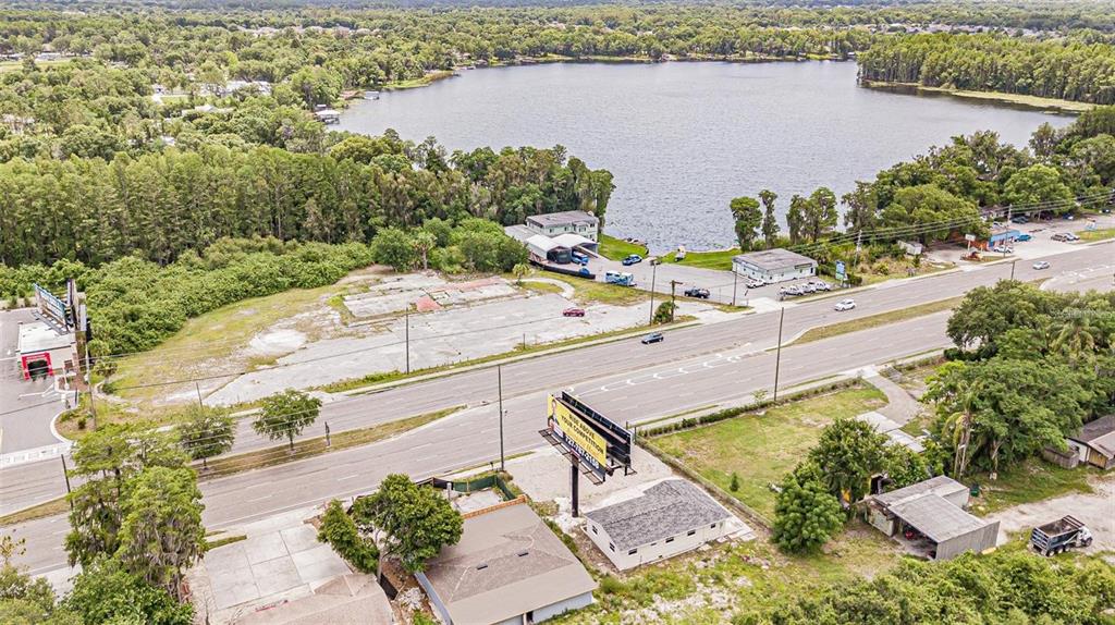 An aerial view shows a vacant lot next to a road, lake, and commercial buildings — 4623 LAND O LAKES BOULEVARD, LAND O LAKES, FL