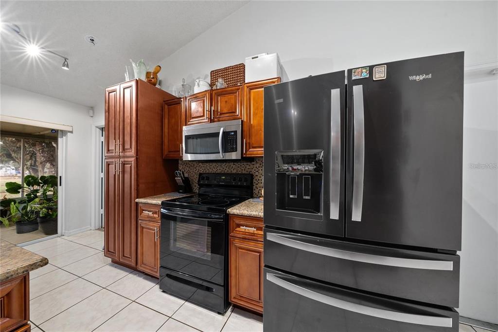 A kitchen features wood cabinets, black appliances, granite countertops, and tile flooring — 22 BOLTON COURT, KISSIMMEE, FL