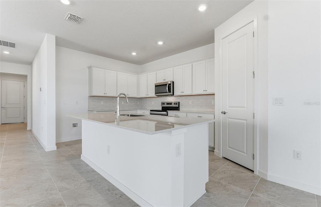 A modern kitchen features white cabinetry, a central island with a sink, and tile flooring — 8132 SW 44TH COURT ROAD, OCALA, FL