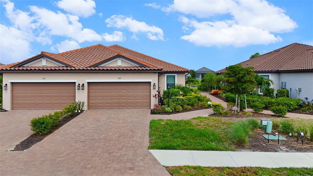 A duplex with two brown garage doors and a paved driveway under a blue sky — 3105 FORMIA COURT, BRADENTON, FL
