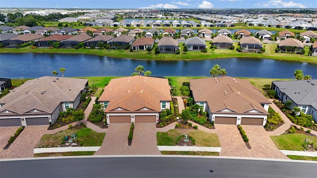 An aerial view shows three suburban houses with tiled roofs and paved driveways near water — 3105 FORMIA COURT, BRADENTON, FL