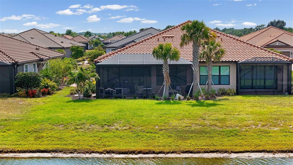 The rear exterior of a house features a screened-in patio, palm trees, and a lawn — 3105 FORMIA COURT, BRADENTON, FL