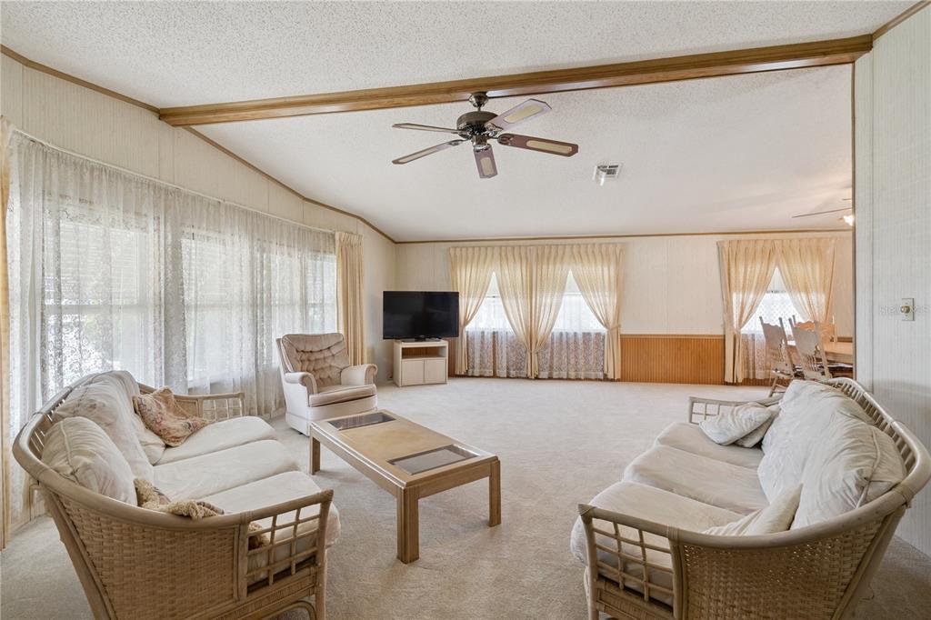 A living room features beige carpeting, wicker furniture, a ceiling fan, and floor-to-ceiling curtains — 5035 LODGEWOOD DRIVE, LAKELAND, FL