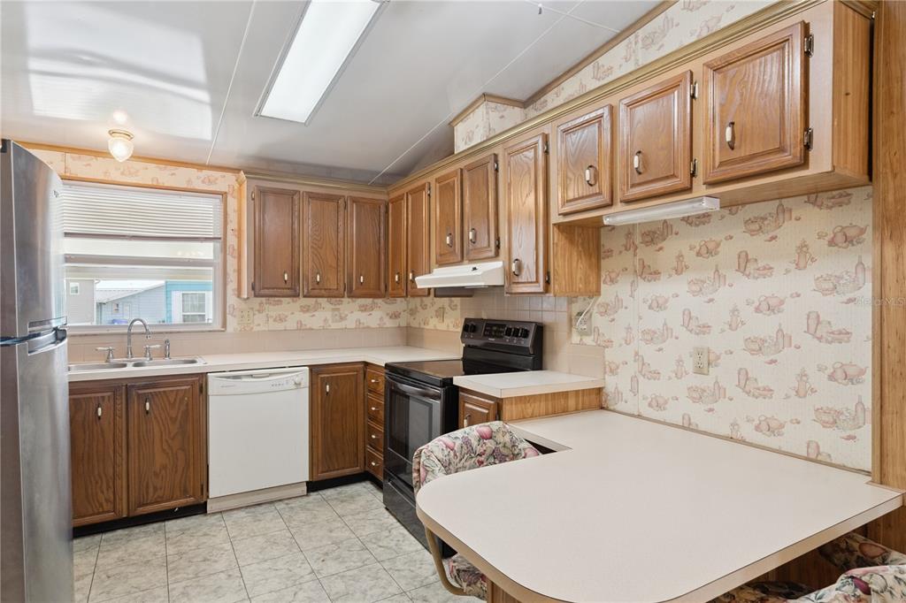 A kitchen features wood cabinets, laminate countertops, a white dishwasher, and patterned wallpaper — 5035 LODGEWOOD DRIVE, LAKELAND, FL