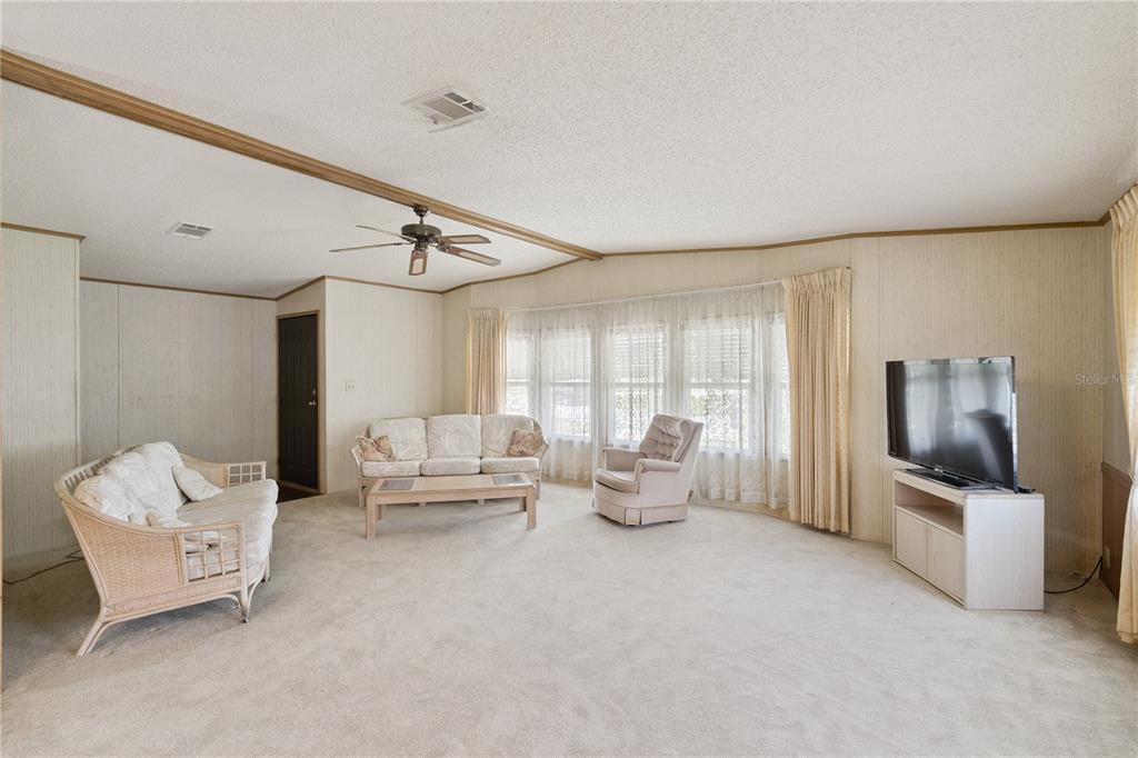 A living room with beige carpet, wood-paneled walls, a ceiling fan, and a bay window — 5035 LODGEWOOD DRIVE, LAKELAND, FL