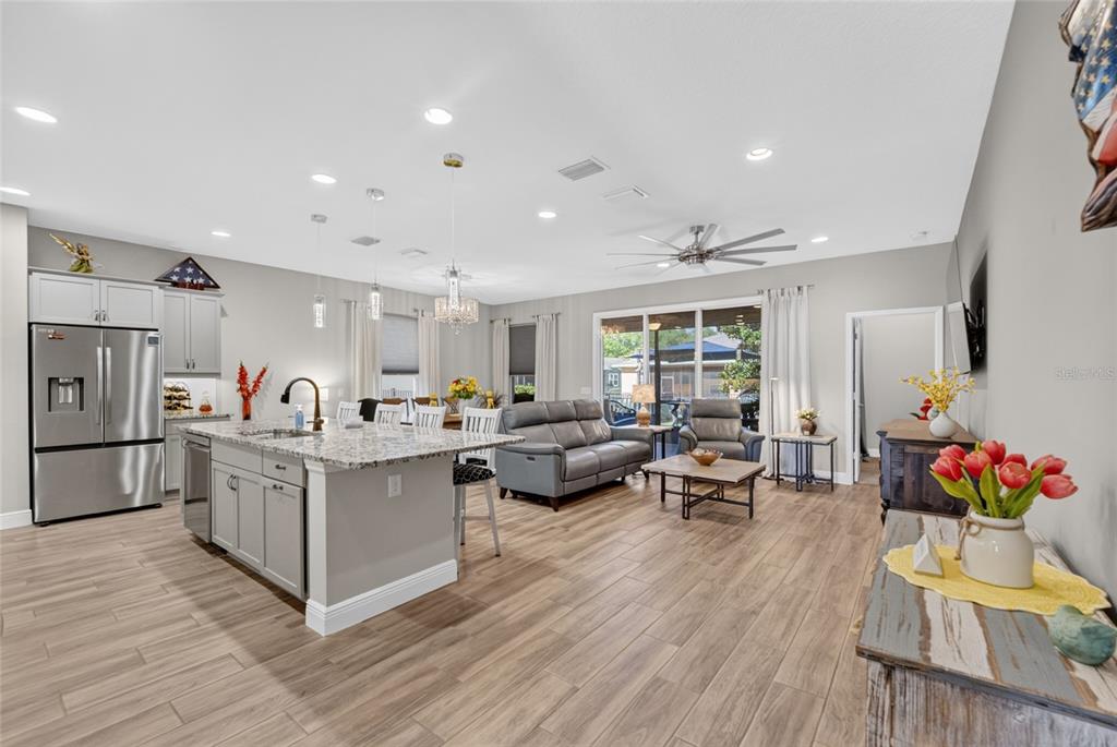 An open-concept kitchen and living area featuring gray cabinetry, granite countertops, and wood-look tile flooring — 3508 NW 55TH COURT, OCALA, FL