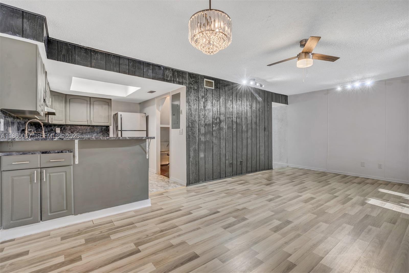 A living room with wood-look flooring, a dark wood-paneled accent wall, and an open kitchen — 94 Pleasant Hill Ln, Tamarac FL 33319, TAMARAC, FL