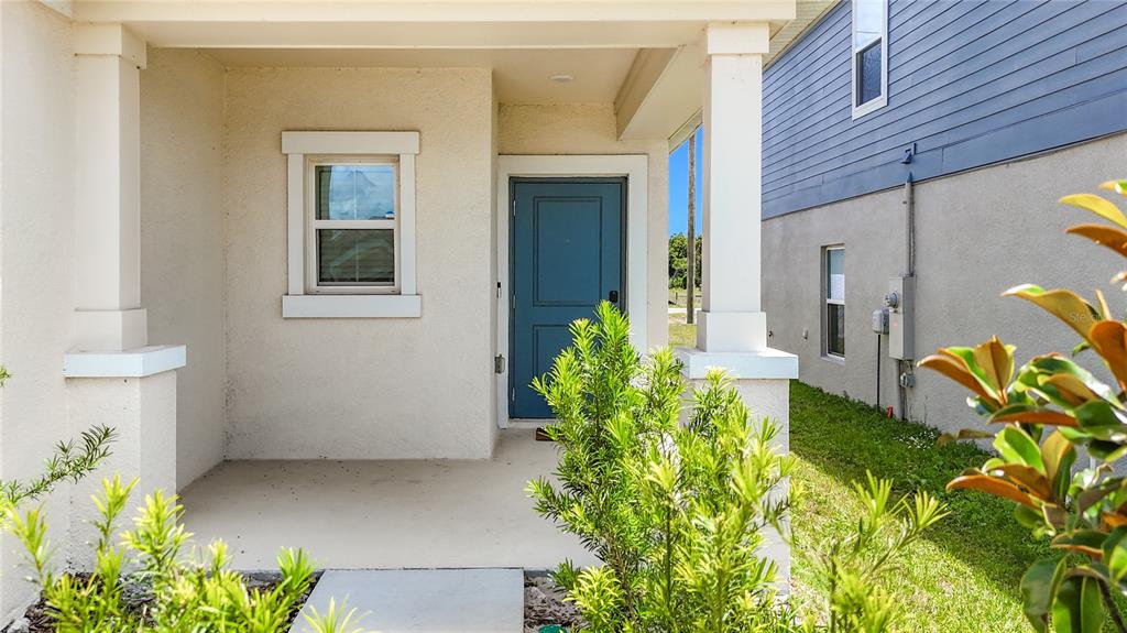 A covered front porch with a blue door and a window on a stucco house — 1688 TEAGAN LANE, WINTER HAVEN, FL