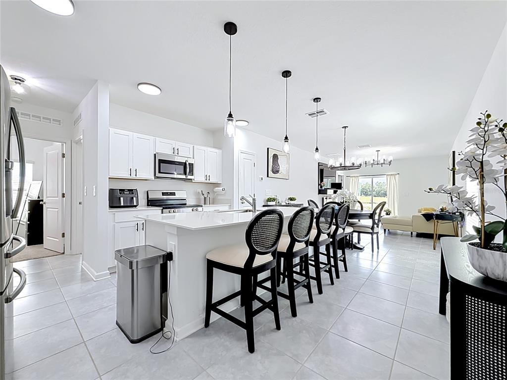 A bright kitchen with white cabinets, a central island with bar stools, and tiled floors — 1688 TEAGAN LANE, WINTER HAVEN, FL
