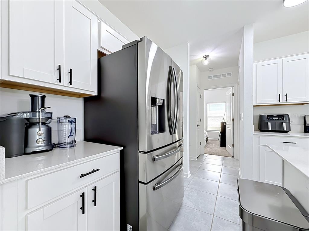 A kitchen features white cabinets, stainless steel appliances, and light tile flooring — 1688 TEAGAN LANE, WINTER HAVEN, FL