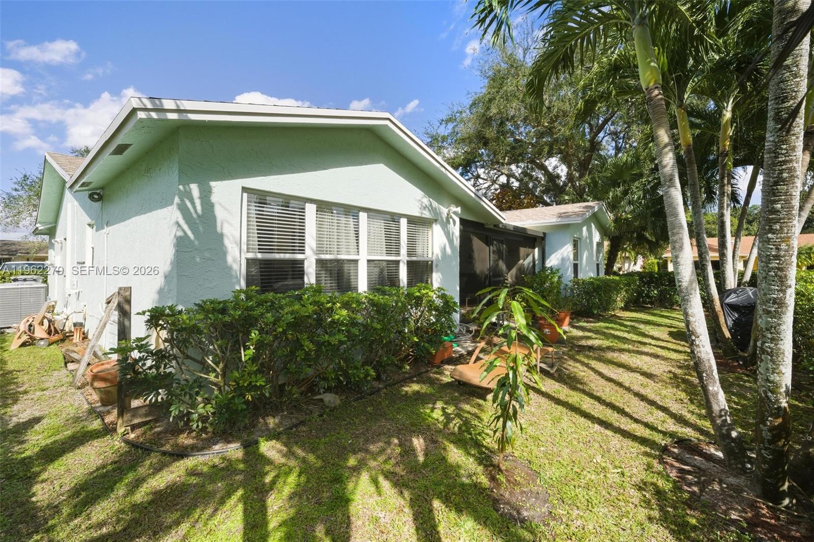 The exterior of a light green house features a large window, landscaping, and palm trees — 10308 Greenbriar Ct, Boca Raton FL 33498, BOCA RATON, FL
