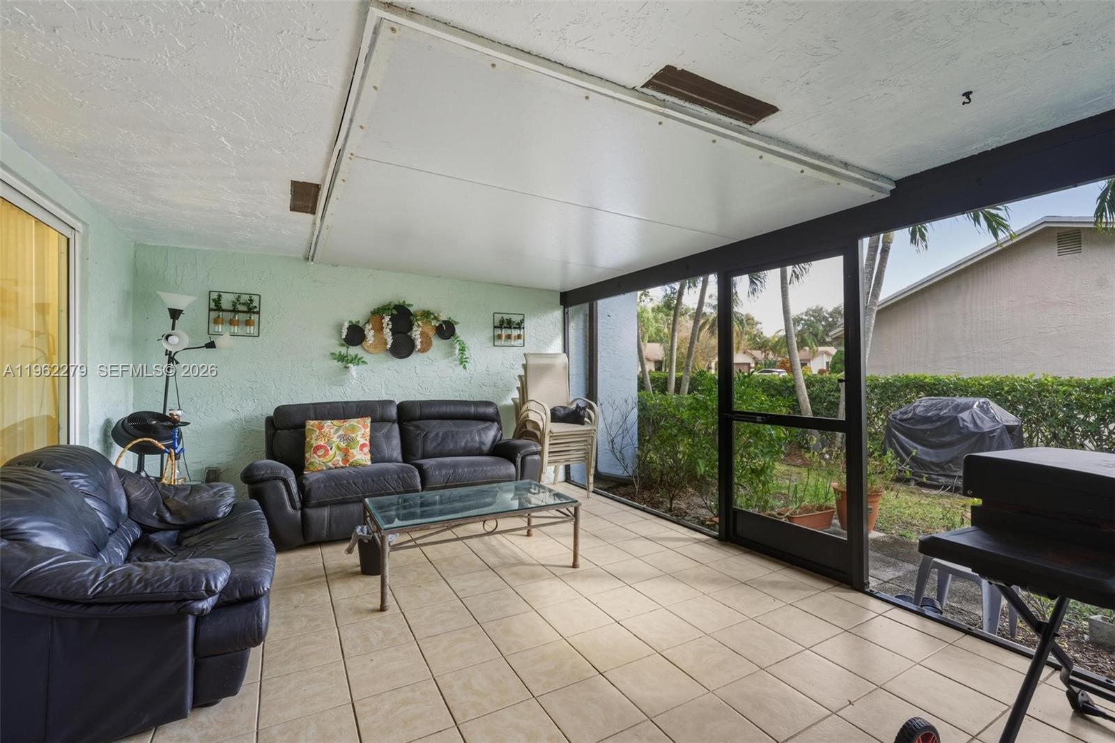 A screened-in patio features tile flooring, a dark leather sofa, and a glass coffee table — 10308 Greenbriar Ct, Boca Raton FL 33498, BOCA RATON, FL