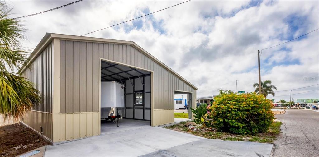 A metal-sided garage with an open bay and a concrete driveway sits under a cloudy sky — 2209 IOWA AVENUE, BRADENTON, FL