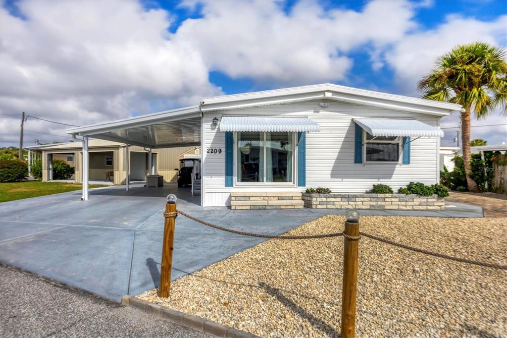 A white manufactured home features a carport, blue shutters, and a gravel front yard — 2209 IOWA AVENUE, BRADENTON, FL