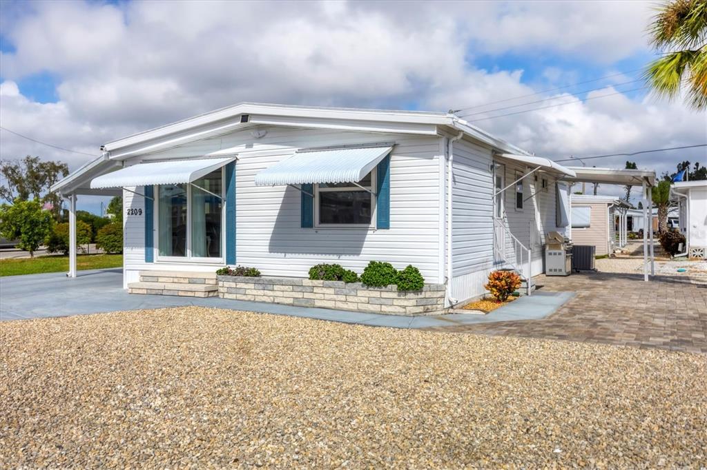 A white mobile home features blue shutters, striped awnings, and a gravel front yard — 2209 IOWA AVENUE, BRADENTON, FL